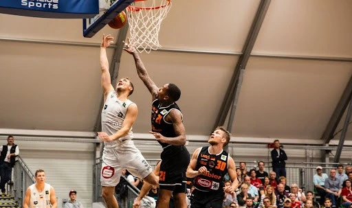 A basketball player attempting to basket while another tries to block.