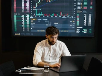 Man in white shirt using his laptop with CAKE/USDT chart projected behind him