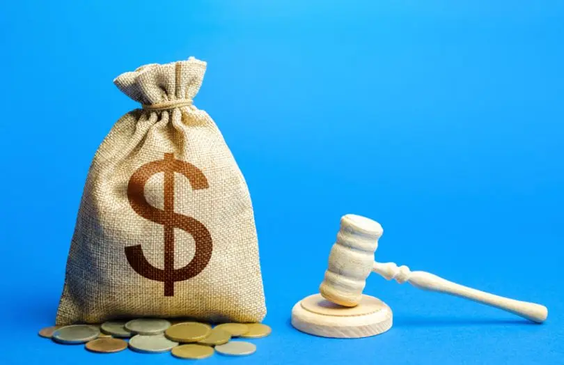 A bag having a dollar symbol printed on it next to a wooden gavel