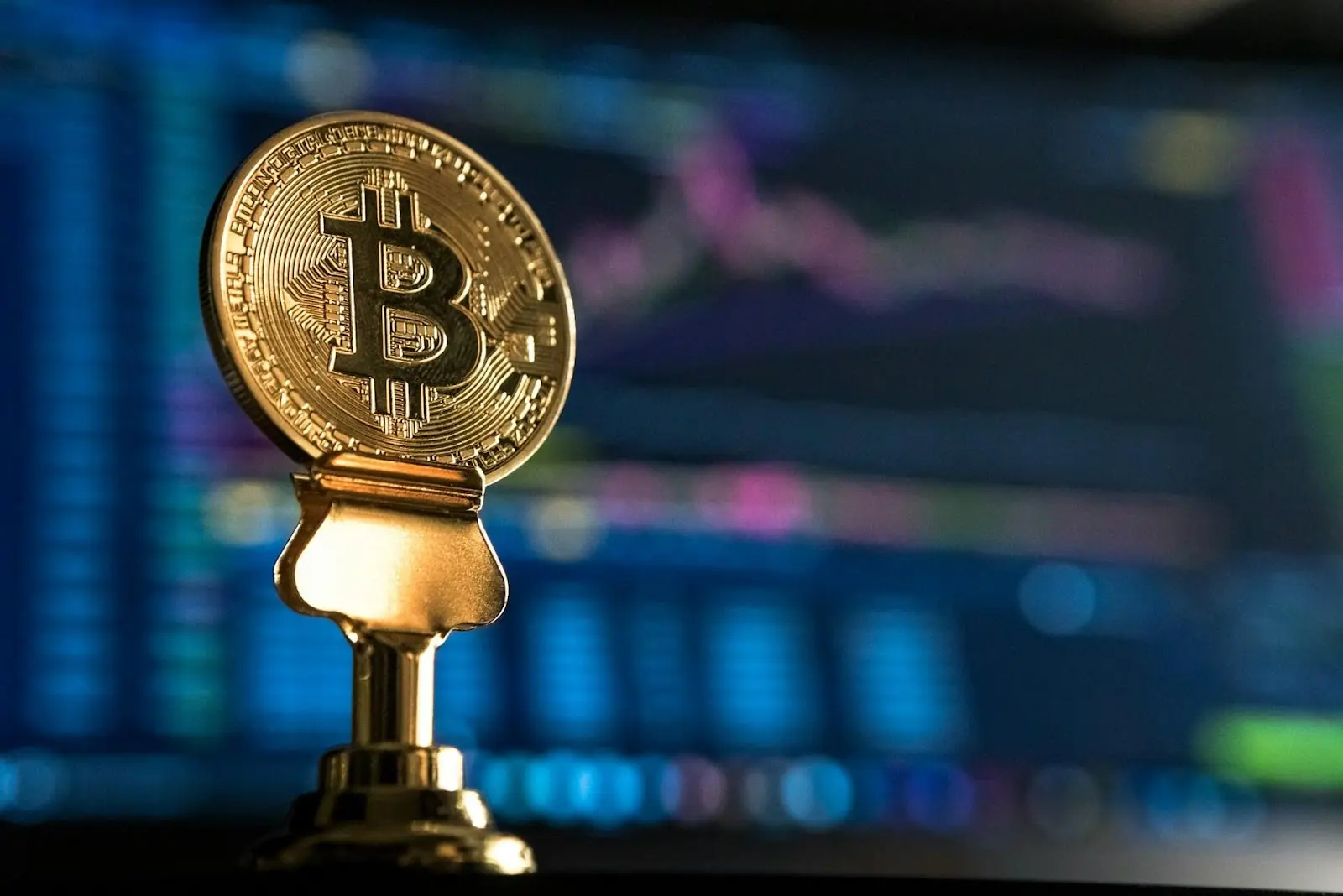  Bitcoin placed in front of a blurred screen with a trading chart